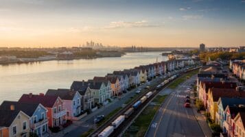 Bayonne NJ waterfront homes and light-rail tracks at sunset with Manhattan skyline in background.